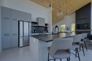 Una cocina moderna con armarios grises, un refrigerador de acero inoxidable, una isla grande con taburetes de bar e iluminación colgante.