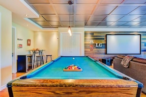 A pool table with balls, a bar area, and a seating area with a TV screen.