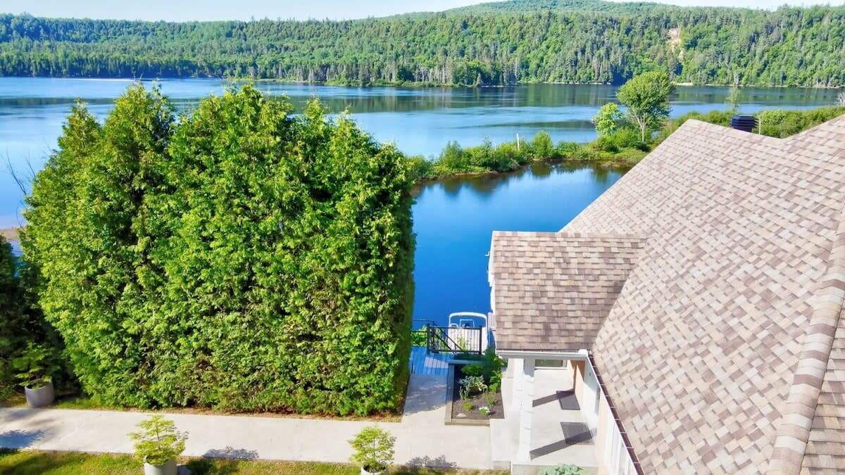 A house with a large green hedge, a view of a lake, and a brick roof.