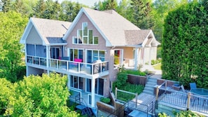 A two-story house with a balcony, a deck, and a large tree in the background.