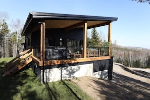 A modern cabin with a covered porch, a staircase, and a view of the surrounding forest.