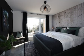 A modern bedroom with a large bed, a view to the outside, a chair, and a plant. - Chalet Le Select - Private Spa with River View (Les Éboulements)