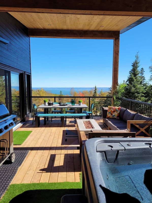 A covered outdoor patio with a grill, seating, and a view of the ocean.