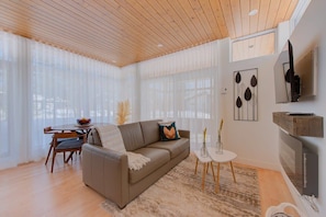 A modern living room with a wooden ceiling, a sofa, a dining table with chairs, a TV, and artwork on the walls. - Le Shalom - Nature & Relax in Pont-Rouge (Pont-Rouge)