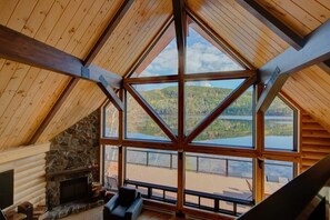 Ein Blockhaus-Interieur mit Kamin aus Stein, einem großen Fenster und Blick auf einen See.