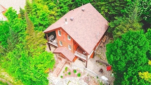 A red wooden house with a balcony, surrounded by dense green trees.