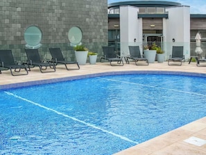 A swimming pool with lounge chairs, potted plants, and a modern building with a brick facade.