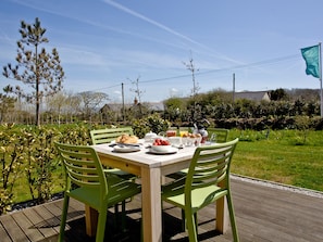 Ein Essbereich im Freien mit einem für das Frühstück gedeckten Tisch, umgeben von Grünpflanzen und blauem Himmel.
