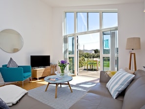 A modern living room with a sofa, a television, a coffee table, and a dining area with chairs.