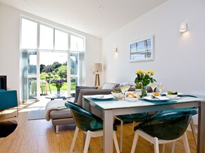 Un coin repas avec une table dressée pour deux personnes, un canapé et une vue sur l’extérieur.