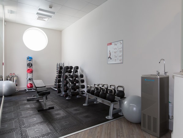Ein Fitnessraum mit Trainingsgeräten, einem Wasserspender und einem Poster an der Wand.