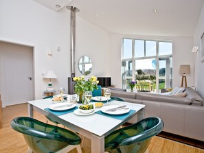 Ein moderner Essbereich mit einem weißen Tisch, grünen Stühlen und einer Couch im Hintergrund.