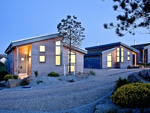A modern two-story house with a gravel driveway, wooden siding, and large windows.
