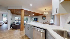 A modern kitchen with a central island, wooden ceiling beams, and a large window offering a view of the outdoors.