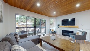 A modern living room with a large sliding glass door, a fireplace, a flat-screen TV, and a cozy seating area.