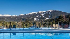 A swimming pool with a mountain backdrop, surrounded by trees and chairs.