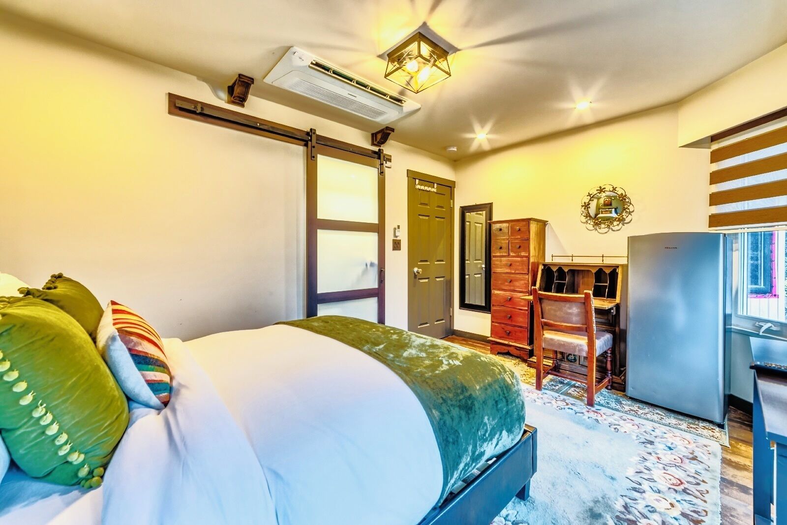 A hotel room with a bed, a desk, a wardrobe, and a refrigerator.