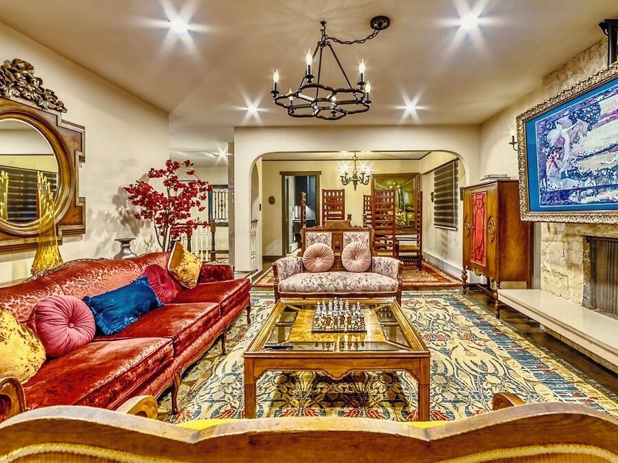 Un salon spacieux avec un canapé rouge, un fauteuil à motifs, une table d’échecs et un grand tableau accroché au mur.