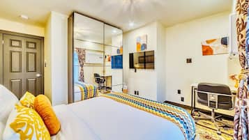 A hotel room with a large bed, a desk, a chair, a television, and a wardrobe.