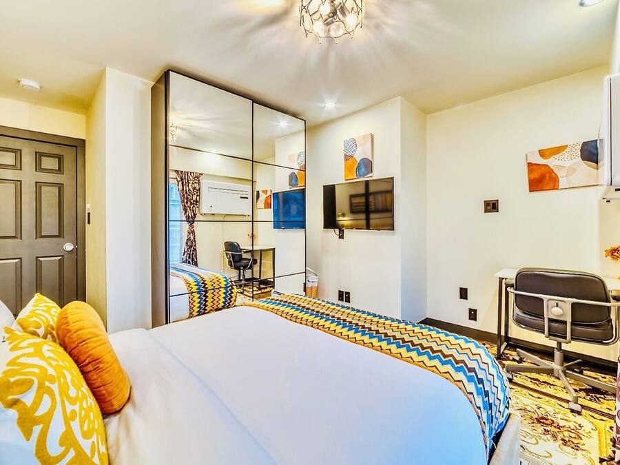 A hotel room with a large bed, a desk, a chair, a television, and a wardrobe.