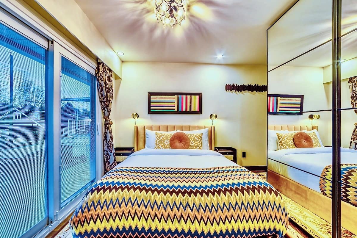 Habitación de hotel moderna con una cama grande, vistas a la ciudad y un espejo que refleja el espacio.