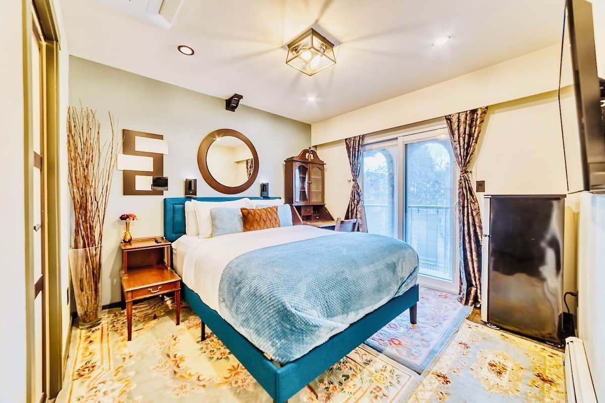 Una habitación de hotel moderna con una cama grande, un espejo, un tocador, un televisor y un balcón con cortinas.