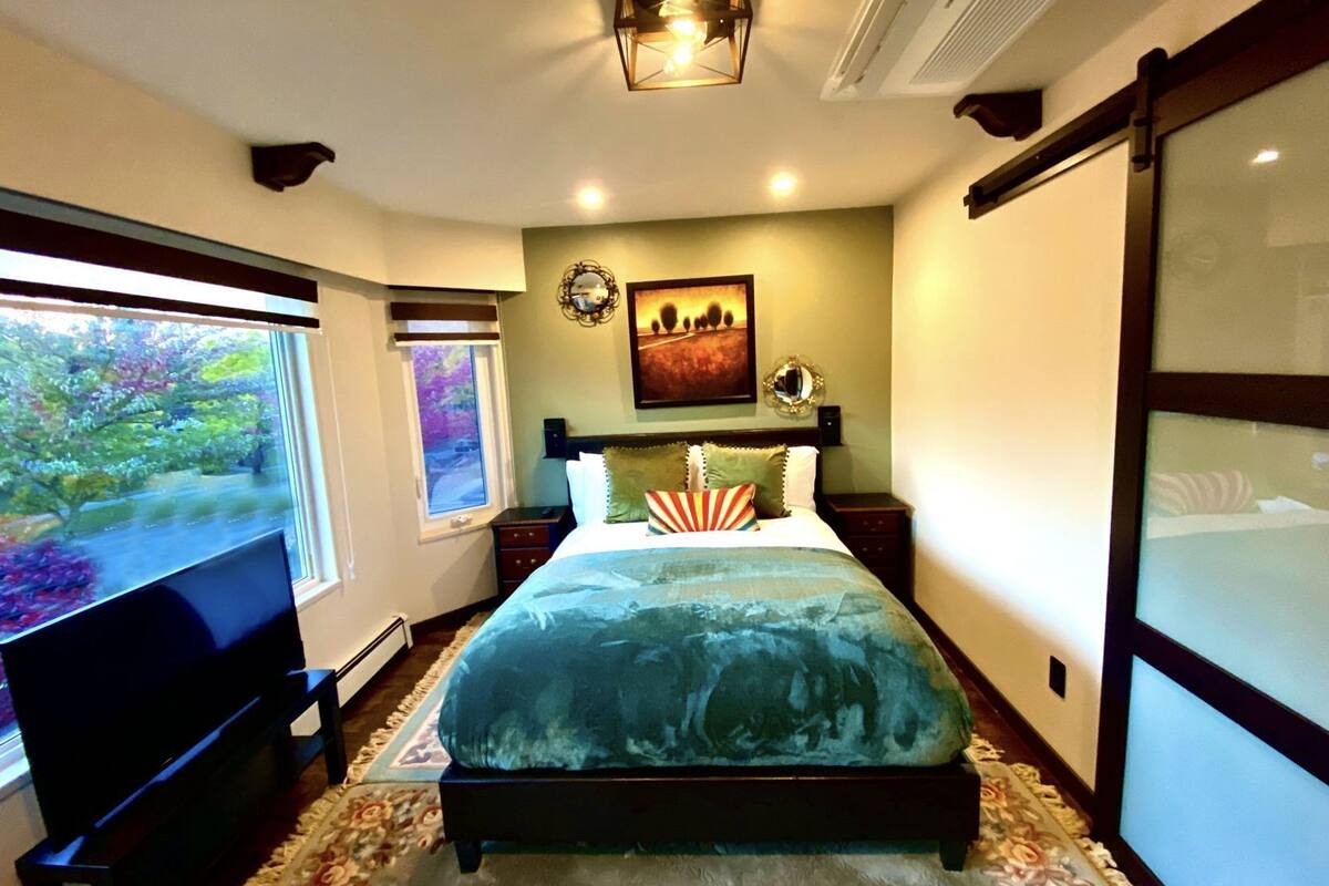 Un dormitorio con cama, televisor, ventana con vistas y un cuadro en la pared.