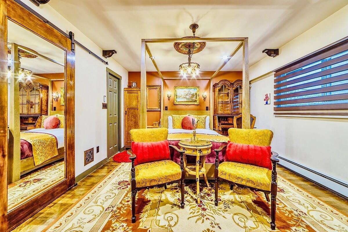 Una habitación con un espejo grande, una araña de cristal, una cama con almohada roja y una alfombra estampada.