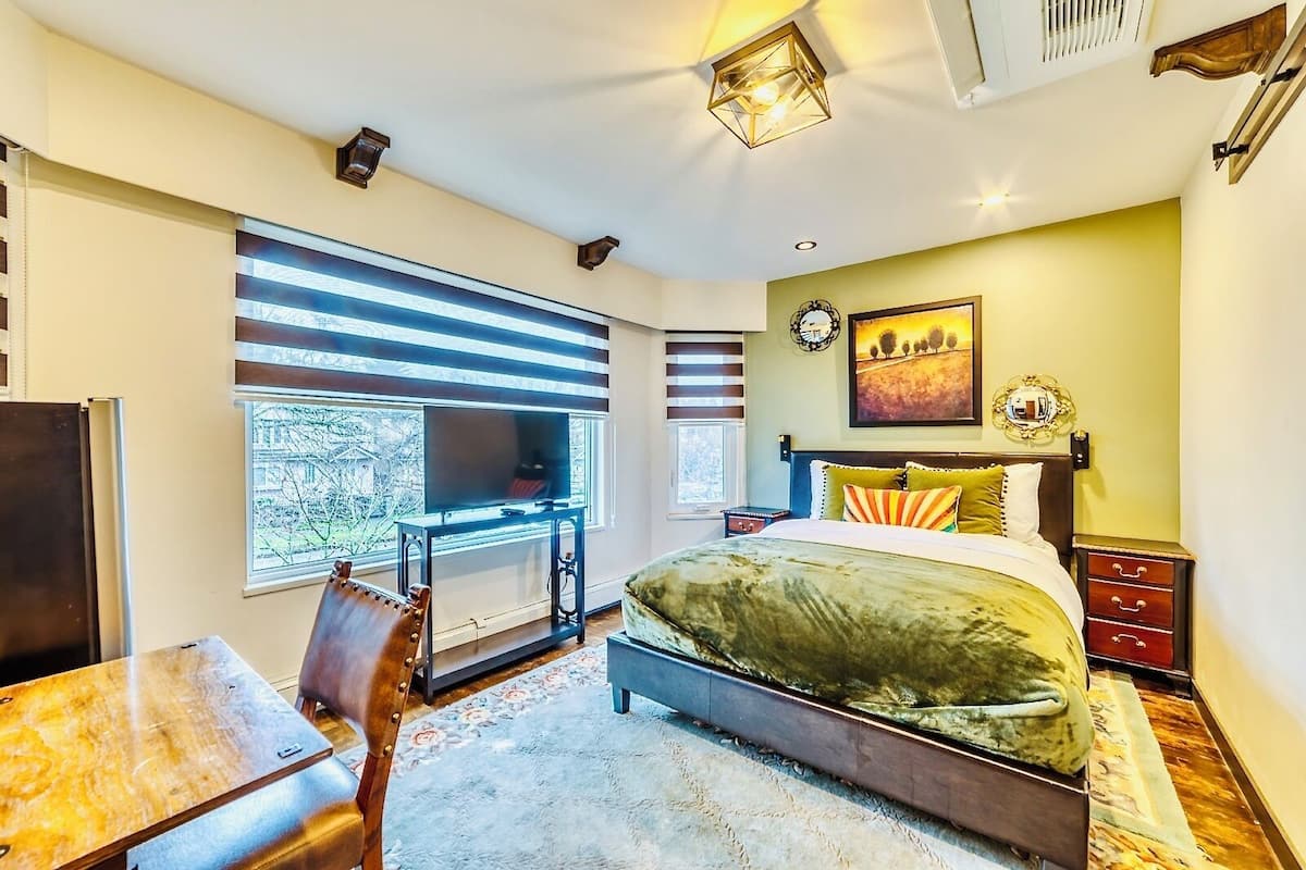 Un dormitorio con cama, escritorio, televisor y ventana con persianas.