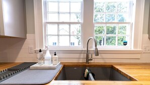 A kitchen with a wooden countertop, a stainless steel sink, and a window with a view of trees. - Edenton Historic District, Walk Downtown, Dogs Welcome, Fenced Yard! (Edenton)