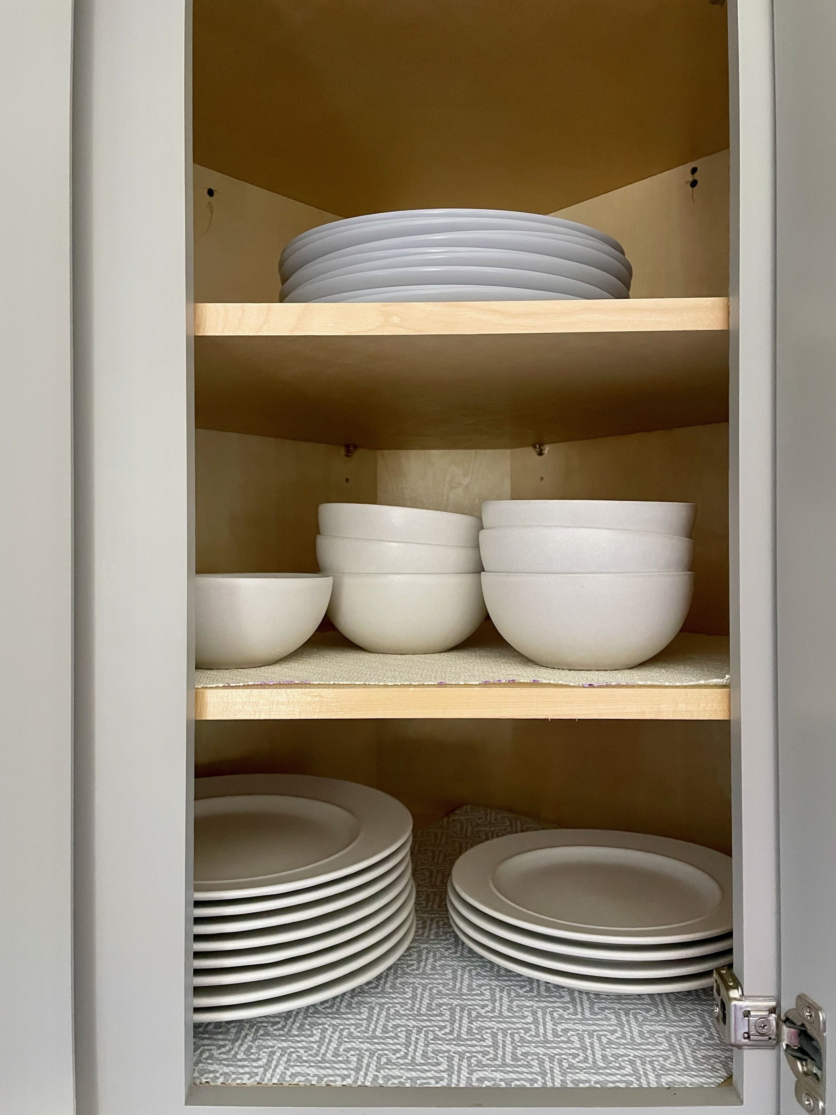 A kitchen cabinet with white bowls and plates.