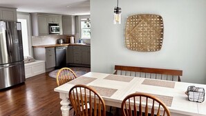A modern kitchen with a dining area, featuring a stainless steel refrigerator, wooden chairs, and a hanging light fixture. - Edenton Historic District, Walk Downtown, Dogs Welcome, Fenced Yard! (Edenton)