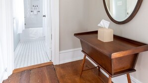 A hallway leading to a bathroom with a wooden floor, a mirror, and a tissue box on a wooden console table. - Edenton Historic District, Walk Downtown, Dogs Welcome, Fenced Yard! (Edenton)