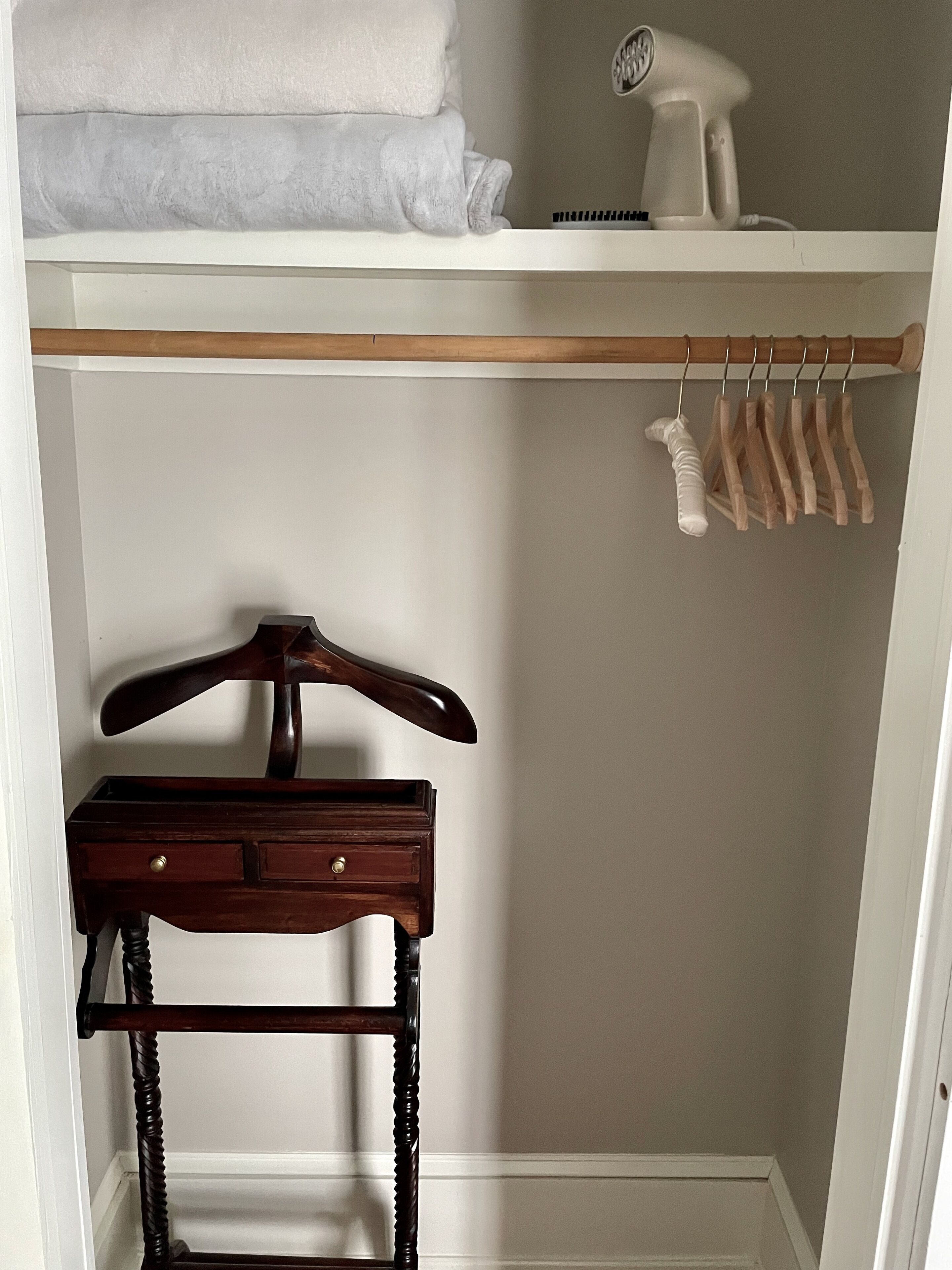 A closet with a wooden hanger rack, a small wooden dresser, and a hairdryer on a shelf.