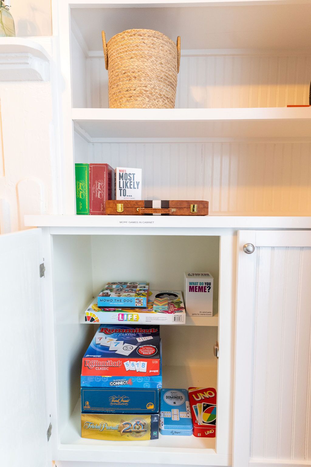 A cabinet with a woven basket on top and various board games and puzzles on the shelves.