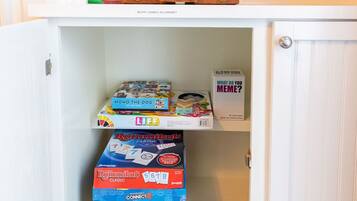 A cabinet with a woven basket on top and various board games and puzzles on the shelves.