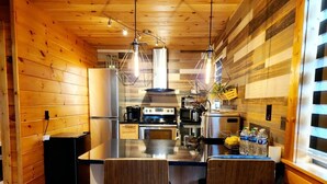 Une cuisine moderne avec des murs en bois, un îlot central doté de tabourets de bar, des appareils en acier inoxydable et un éclairage suspendu.
