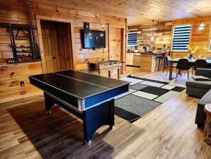 A cozy room with a ping pong table, a foosball table, and a TV mounted on the wall.