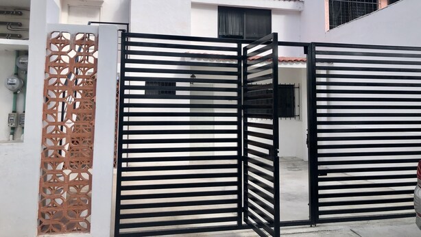 A gated entrance with a decorative metal gate and a white building with a tiled roof.