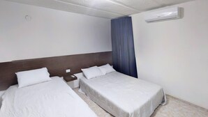 A hotel room with two beds, a wooden headboard, a nightstand, a wall-mounted air conditioner, and a blue curtain.