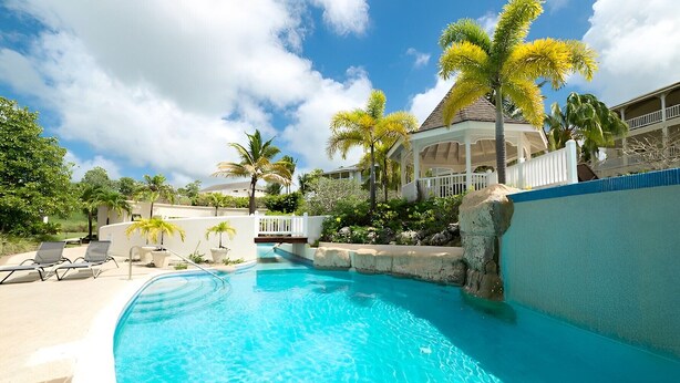A clear blue pool with lounge chairs, palm trees, and a house in the background.