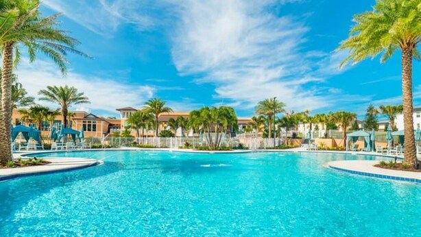 A large outdoor swimming pool surrounded by palm trees and buildings.