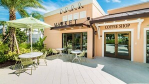 A building with a 'MARKET' sign and a 'COFFEE SHOP' sign. There are outdoor tables and chairs.