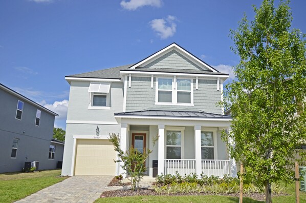 A two-story residential house with a front porch, a garage, and a small garden area. - Cheerful 8 Bedroom Vacation Home with Pool/Games (Four Corners)