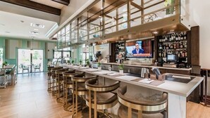 A modern bar area with a long counter, multiple stools, and a television screen.