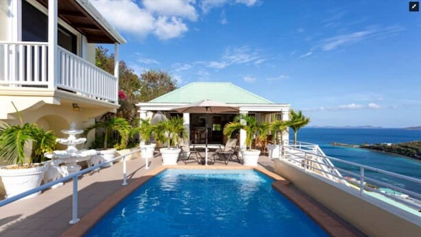 A pool area with a view of the ocean, a covered seating area, and a building with a balcony. - Villa Rosa (West End)