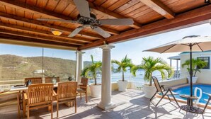 A covered outdoor area with a pool, wooden furniture, and potted plants. - Villa Rosa (West End)