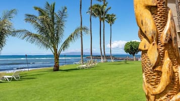 A beach view with palm trees, a wooden sculpture, and lounge chairs.