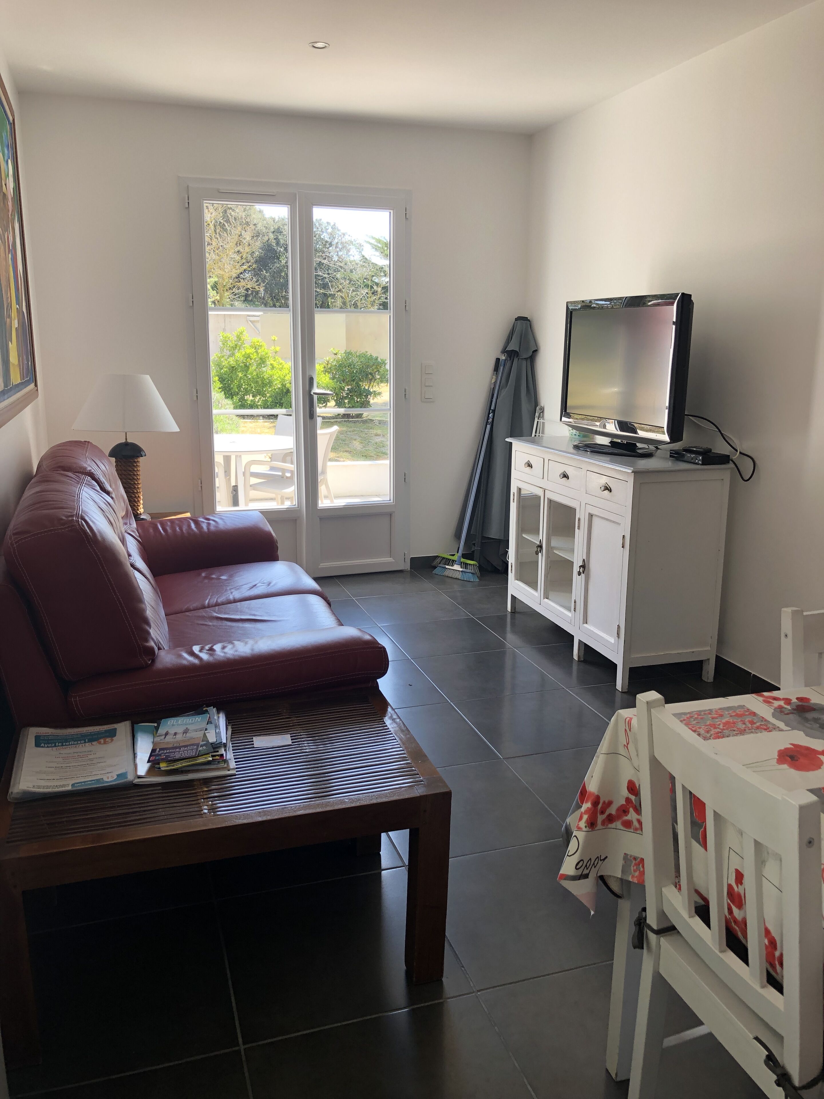 A living room with a leather sofa, a coffee table with books, a television on a cabinet, and a sliding glass door leading to an outdoor area.