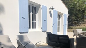 En uteplats med utemöbler och en vit byggnad med blåa fönsterluckor.